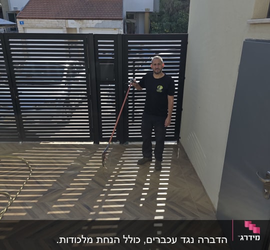 אדם מחזיק כלי עבודה בחצר עם שער ברקע